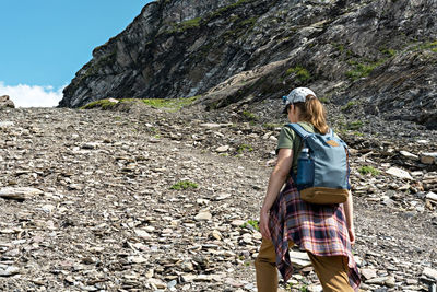Rear view young woman with backpack walking uphill along rocky trail in mountain hike , hiking