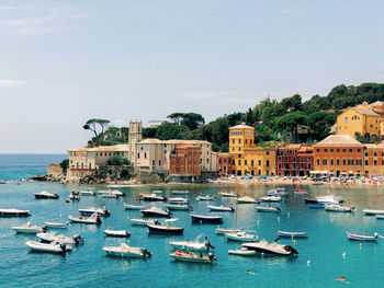 Sailboats moored on sea by buildings in city against sky