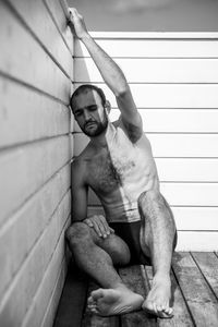 Full length of shirtless man sitting by wall