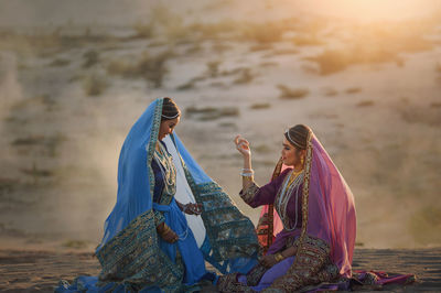 Female friends wearing traditional clothing kneeling on land