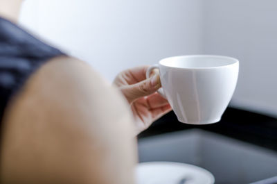 Cropped image of woman holding white coffee cup at home