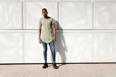 Serene african american male in stylish clothes standing with closed eyes near modern building and enjoying sunny weather
