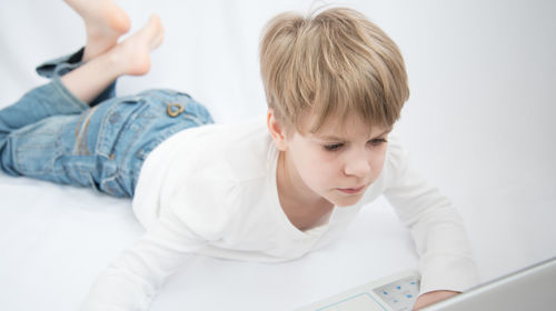 Cute boy looking away while relaxing on bed at home