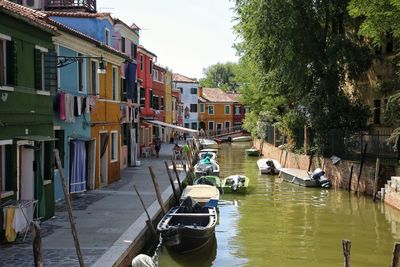 Boats moored in canal by city against sky