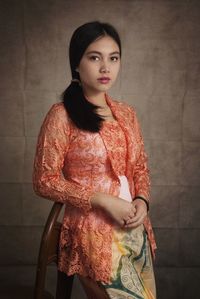 Portrait of young woman standing in traditional clothing standing against wall