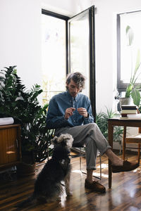 Full length of male architect talking with dog while sitting at home office