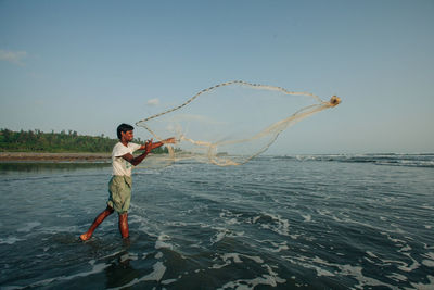 Full length of fisherman fishing in sea against sky