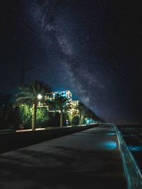 Illuminated street amidst buildings against sky at night