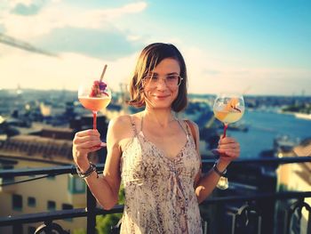 Portrait of smiling woman holding ice cream against sky