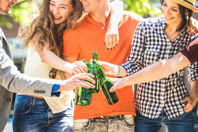 Friends toasting beer bottles while standing outdoors