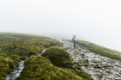 Scenic view of path on grassy hill in foggy weather