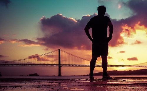 Silhouette of man standing on bridge at sunset