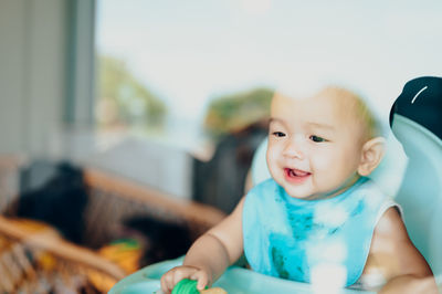 Cute baby boy sitting on high chair seen through window