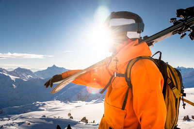 Portrait of a man holding skis on his shoulder and looking at a snowy mountain against the backdrop