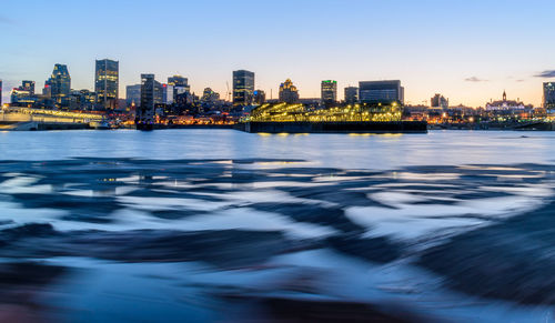 Illuminated buildings by river against sky in city