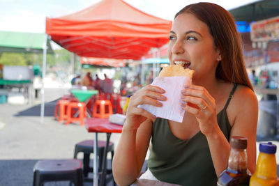 Beautiful young woman eating brazilian traditional food pastel de feira in sao paulo, brazil