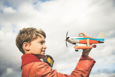 Boy playing with toy airplane against sky