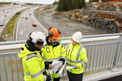 Engineers in reflective clothing discussing plans on viaduct