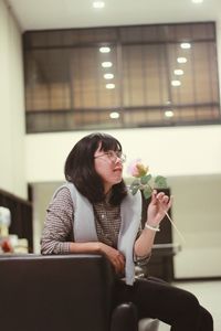 Young woman holding flower while sitting at home