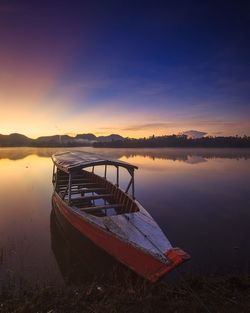 Boat moored on lake against sky during sunset