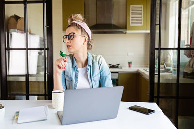 Woman looking away while sitting by laptop at home