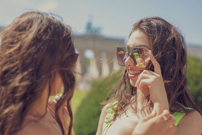 Fashionable young woman wearing sunglasses by friend in city during sunny day