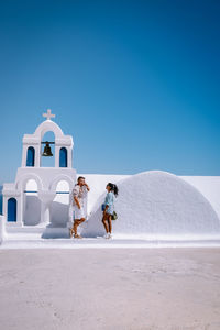 People walking by sea against clear blue sky