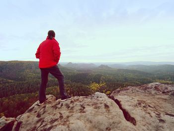 Hiker standing on a rocky mountain summit, watching the morning mist and the rising sun at dawn