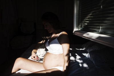 Young woman looking down while sitting on window