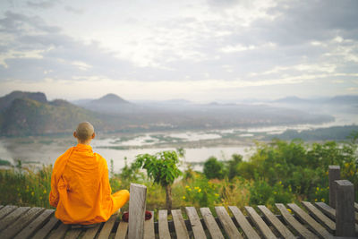 Monk sitting on boardwalk against landscape