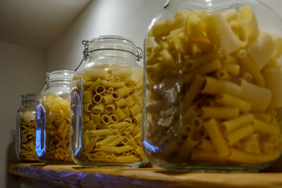 Four glass jars standing on the shelf and filled with various types of pasta.