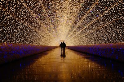 Silhouette couple with umbrella walking in illuminated corridor during rainy season