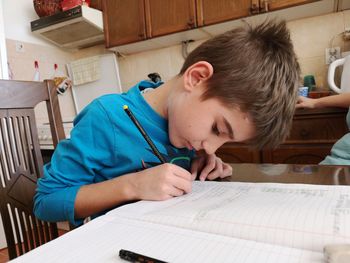 Cute boy writing in book at home