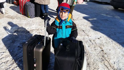 Portrait of boy with luggage standing on snow
