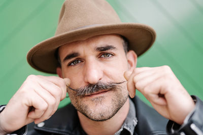 Mature male in leather jacket curling mustache while looking at camera standing on green gate