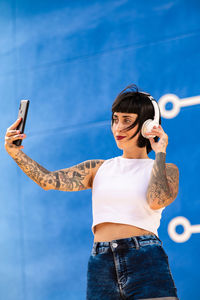 Caucasian girl with tattoos on her body listening to music with headphones on the street