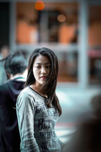 Portrait of young woman standing against blurred background