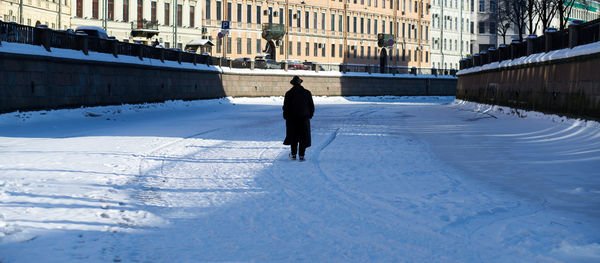 Rear view of man walking on snow covered city in winter