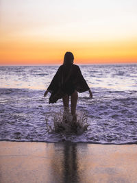 Rear view of woman splashing in sea at dusk