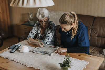 Home caretaker and senior woman solving crossword puzzle