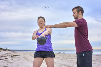 Friends exercising at beach against sky