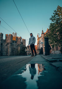 Rear view of man walking by buildings against sky in city