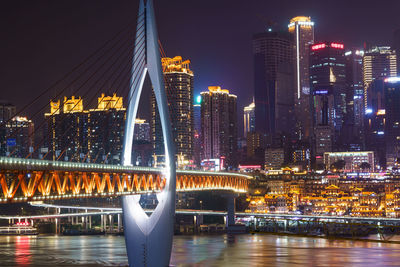 Illuminated bridge over river by buildings in city at night