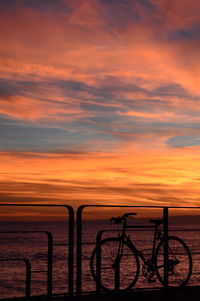 Silhouette bicycle by sea against sky during sunset