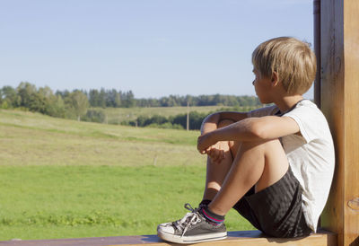 Boy looking away while sitting on wood