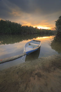 Boat moored on shore against sky during sunset