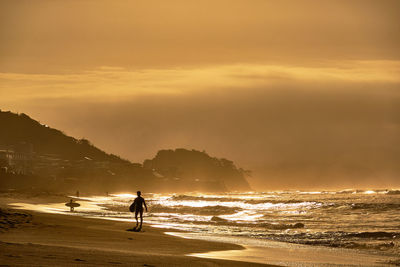 Silhouette woman on beach against sky during sunrise