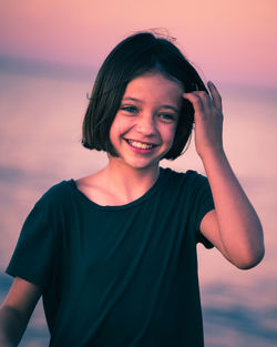 Close-up of smiling girl standing against sea during sunset