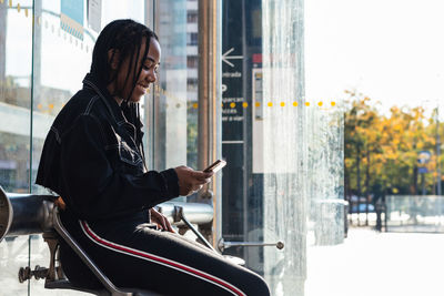 Rear view of man using mobile phone while sitting on window