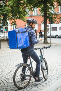 Food delivery man with bicycle using smart phone on street in city